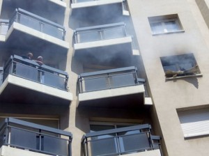 Imatge de veïns als balcons de l'immoble afectat per l'incendi, amb el fum sortint d'una de les finestres. Foto: ACN