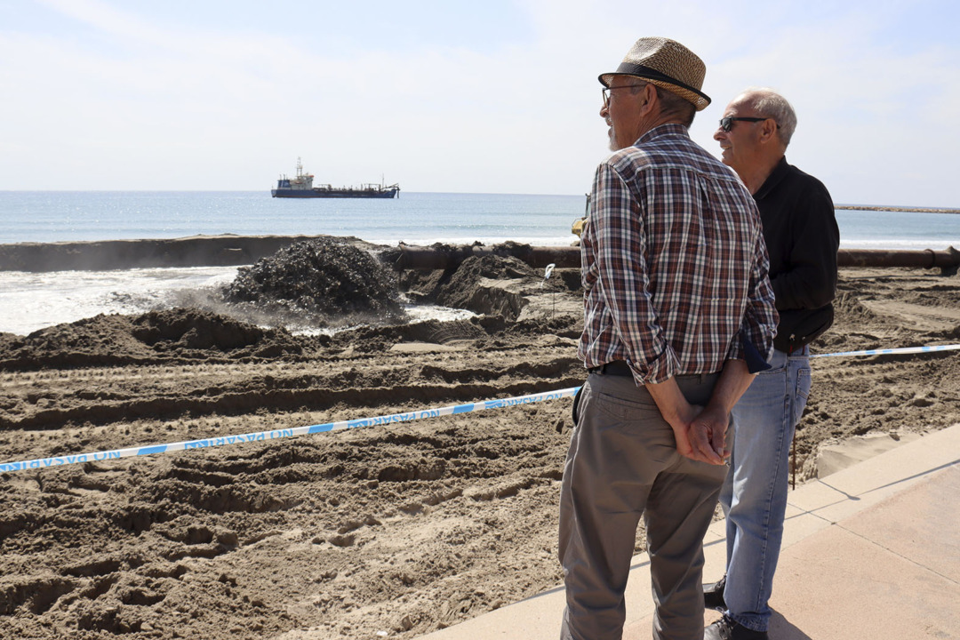 Dues persones mirant les tasques de reposició de sorra a la platja de la Pineda. Foto: ACN