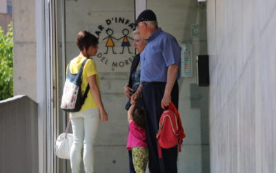 Uns avis amb una nena, d'esquena, parlant amb una dona a la porta de la llar d'infants municipal d'El Morell. Foto: ACN